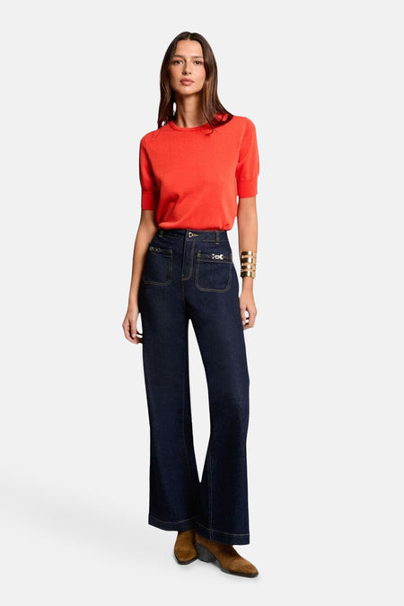 Maillot orange avec col rond de Morgan De Toi, associé à des jeans foncés avec des jambes larges et un bracelet doré.