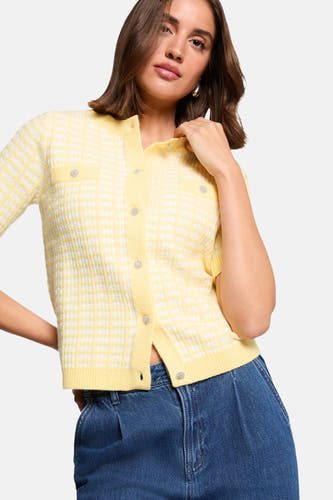 Gele cardigan van Morgan De Toi, met een wit ruitpatroon, korte mouwen en decoratieve knopen, gecombineerd met een donkerblauwe jeans.
