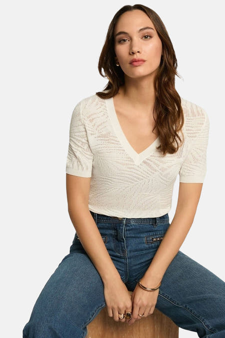 Witte V-hals trui van Morgan De Toi met opengebreid patroon en korte mouwen, gecombineerd met blauwe jeans.
