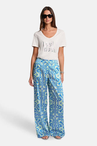 T-shirt blanc à manches courtes de Morgan De Toi, avec le texte 'Feel Good' et porté avec un pantalon bleu imprimé.