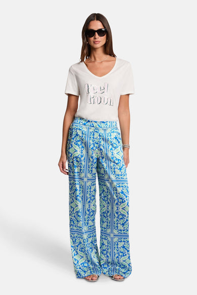 T-shirt blanc à manches courtes de Morgan De Toi, avec le texte 'Feel Good' et porté avec un pantalon bleu imprimé.