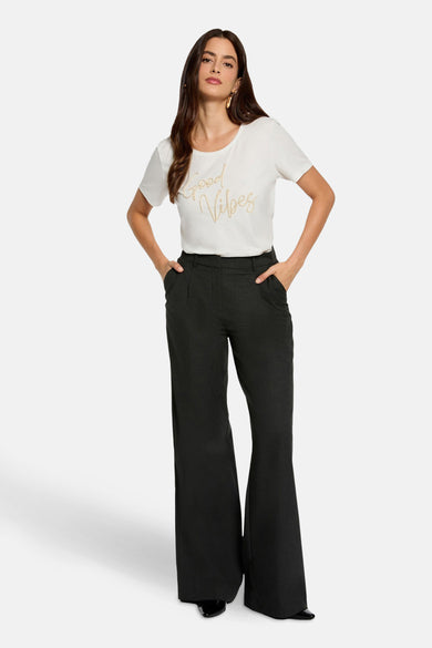 T-shirt blanc à manches courtes de Morgan De Toi, avec un imprimé 'Good Vibes' doré, associé à un pantalon noir.