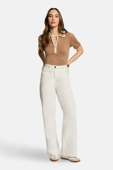 Beige polo met korte mouwen van Morgan De Toi, met witte details en gedragen met een witte broek.

