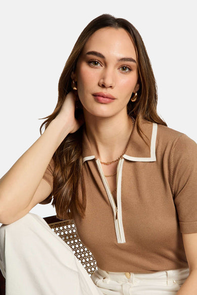 Beige polo met korte mouwen van Morgan De Toi, met een witte kraag en ritssluiting, gecombineerd met gouden sieraden.
