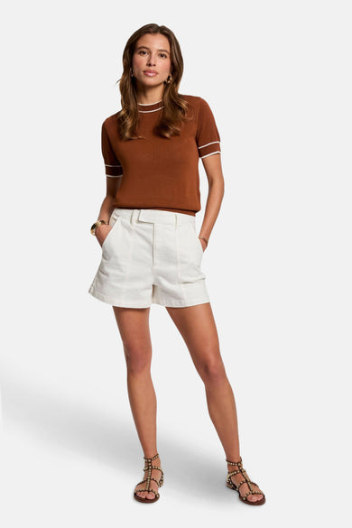 Bruine trui met ronde hals van Morgan de Toi, met witte boorden, gecombineerd met een witte shorts en sandalen met studs.
