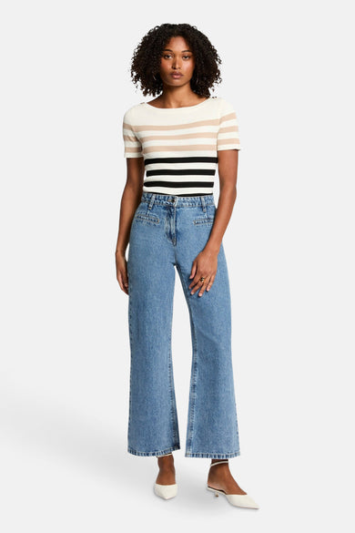 Pull écru à col rond de Morgan de Toi, avec des rayures beige et noires, associé à des jeans larges et des escarpins blancs.