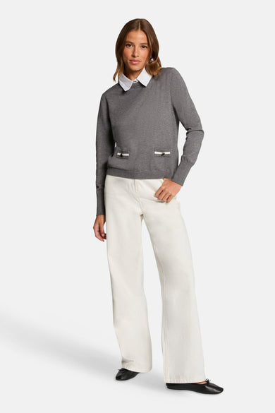 Grijze trui met rolkraag van Morgan De Toi, met sierlijke zakken en gedragen met een witte blouse en wijde, witte broek.