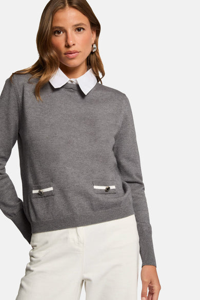 Grijze rolkraagtrui van Morgan De Toi, met decoratieve zakken en gedragen met een wit overhemd en een witte broek.
