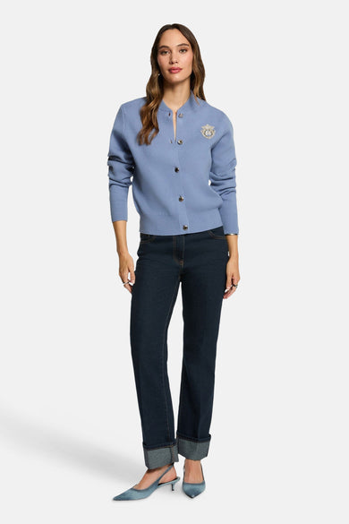 Blauw gilet van Morgan De Toi, met knoopsluiting en decoratieve broche, gecombineerd met donkere jeans en blauwe pumps.
