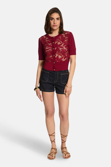 T-shirt rouge à col rond de Morgan De Toi, avec un imprimé floral et porté avec des shorts en jeans et des sandales à lacets.