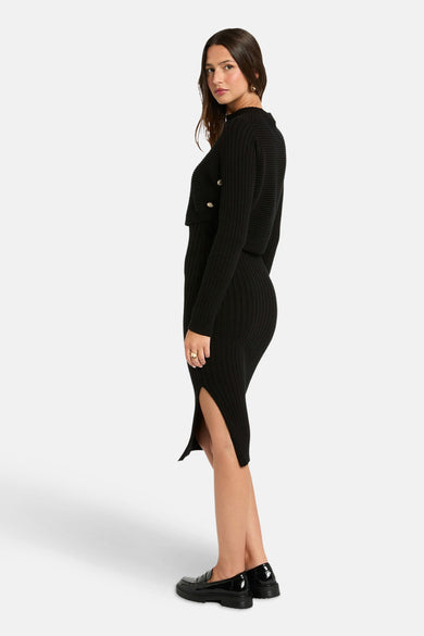 Robe noire à longues manches de Morgan De Toi, avec des boutons sur le gilet et une fente sur le côté.