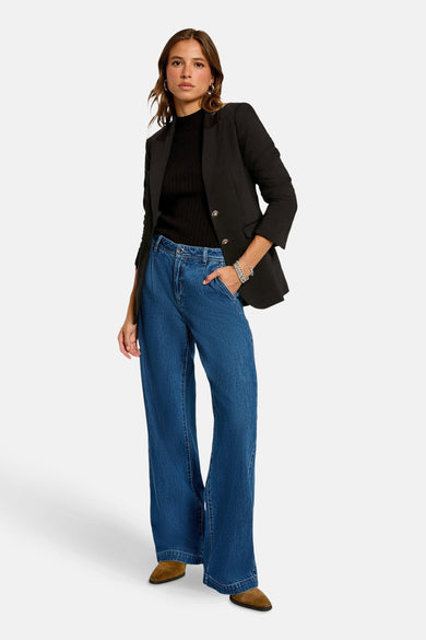 Zwarte blazer van Morgan De Toi, gedragen over een zwarte coltrui en blauwe wijde pijpen jeans, met bruine schoenen.

