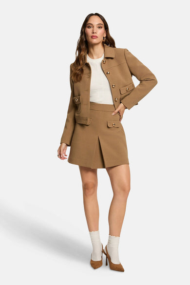 Manteau beige de Morgan De Toi, avec des boutons dorés, porté avec une jupe coordonnée et des chaussettes blanches.