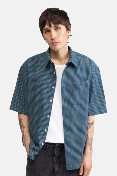 Chemise verte à fines rayures et manches courtes de REDEFINED REBEL, portée ouverte sur un t-shirt blanc par un homme tatoué.