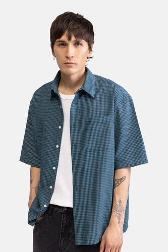 Chemise verte à manches courtes de REDEFINED REBEL, à motif à fines carreaux, portée ouverte sur un t-shirt blanc.