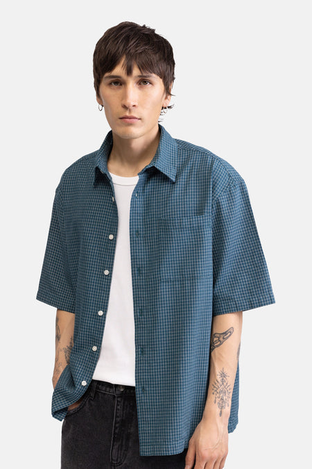 Chemise verte à manches courtes de REDEFINED REBEL, à motif à fines carreaux, portée ouverte sur un t-shirt blanc.