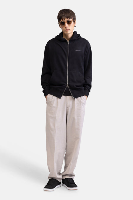 Ecru broek van REDEFINED REBEL, losvallend, gedragen door een man met een zwarte hoodie en sneakers.