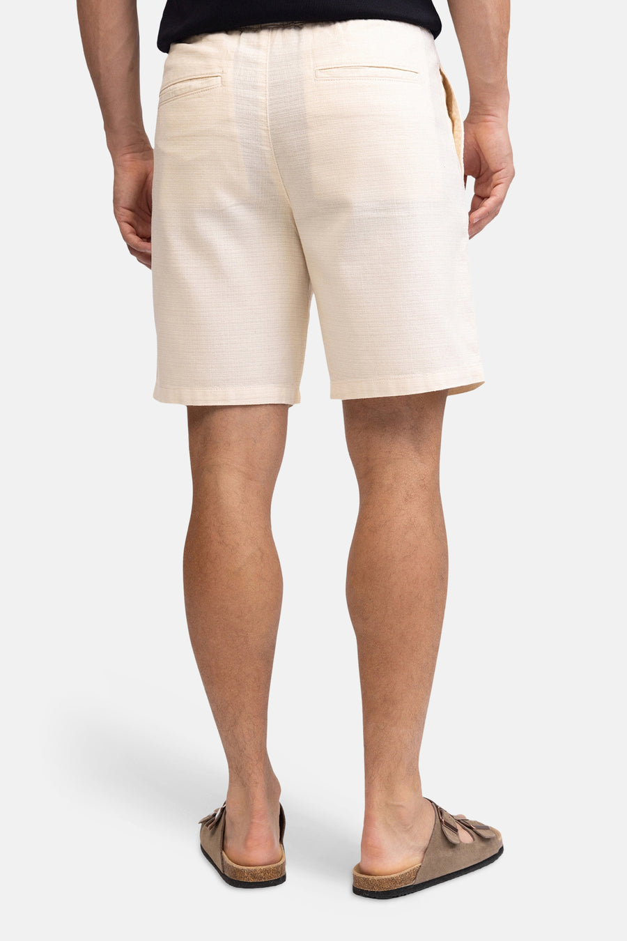Ecru linnenlook short van REDEFINED REBEL, gezien van achteren, met elastische tailleband en paspelzakken, gedragen door een man met bruine sandalen.