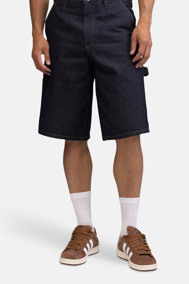 Donkerblauwe denim jeansshorts van REDEFINED REBEL, rechte pasvorm, met zakken en bruine naden, vooraanzicht op model met witte sokken en bruine sneakers