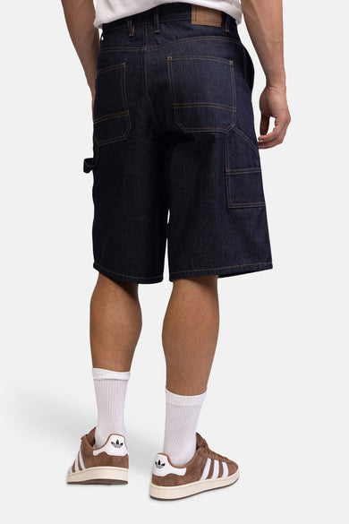 Donkere denim jeansshorts van REDEFINED REBEL, achterzijde met grote zakken, bruine naden, model draagt witte sokken en bruine sneakers