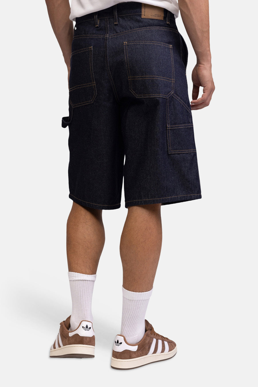 Donkere denim jeansshorts van REDEFINED REBEL, achterzijde met grote zakken, bruine naden, model draagt witte sokken en bruine sneakers
