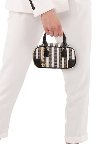 Zwarte schoudertas van Morgan De Toi met strepenpatroon en gouden "M" bedel, gedragen met een witte broek en blazer.
