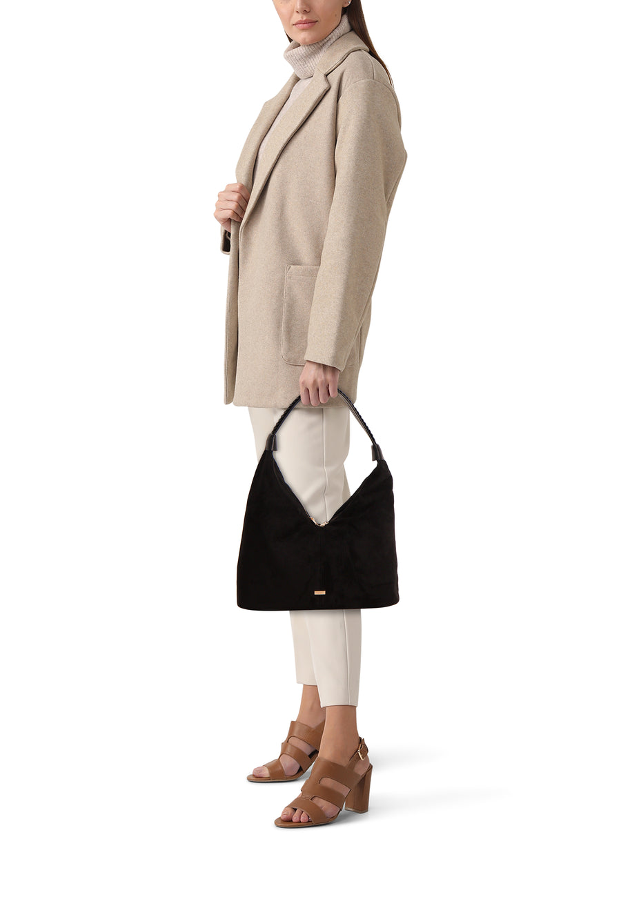 Zwarte schoudertas van Morgan De Toi, met gevlochten handvat, gedragen met beige broek, trui en jas, en bruine hakken.