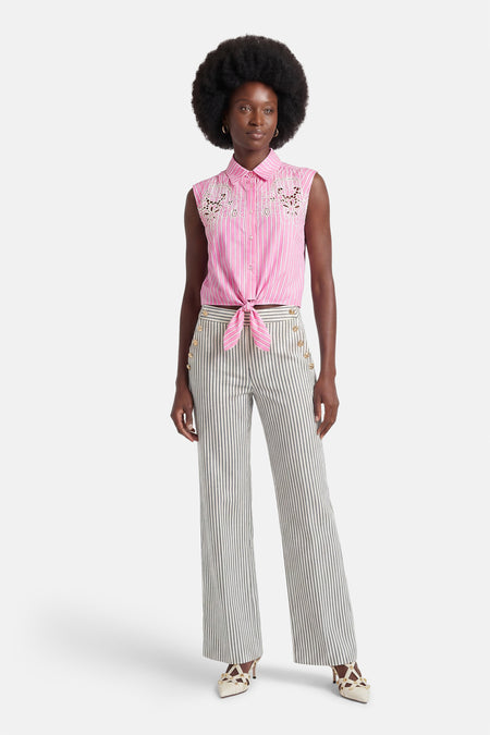 Roze gestreept hemd met korte mouwen van Morgan De Toi, met opengewerkt borduursel en geknoopt in de taille, gedragen met gestreepte broek en beige hakken.
