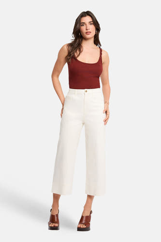 Haut de couleur brique (bretelles spaghetti) de Morgan De Toi, avec des fines bretelles et porté avec un pantalon blanc et des talons marron.