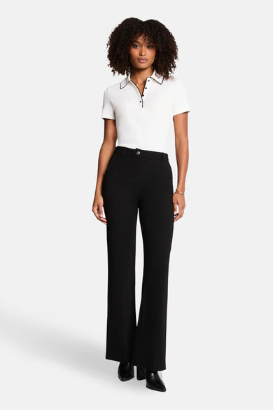 Witte polo met korte mouwen van Morgan De Toi, afgewerkt met zwarte randen en gedragen met zwarte pantalon en laarsjes.