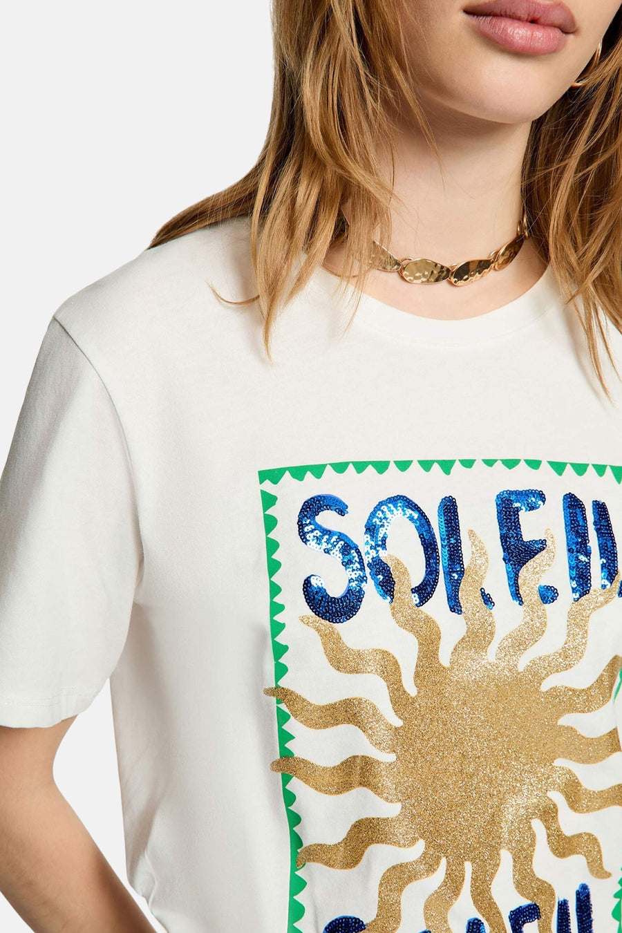 T-shirt blanc Morgan De Toi avec 'SOLEIL' en sequins bleus et un soleil à paillettes dorées, encadré d'un bord festonné vert.