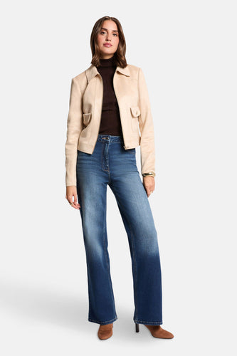 Vrouw in jeans, bruine coltrui, beige jas en laarzen.