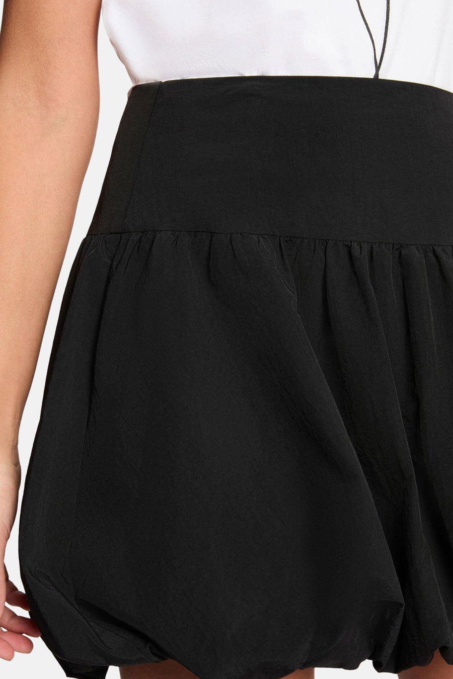 Jupe courte noire de Morgan De Toi, avec une silhouette bouffante et associée à un t-shirt blanc et des talons noirs.
