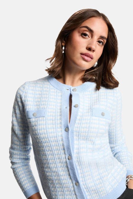 Blauw vest van Morgan De Toi, met ruitpatroon en sierknopen, op een model met zilveren oorbellen.
