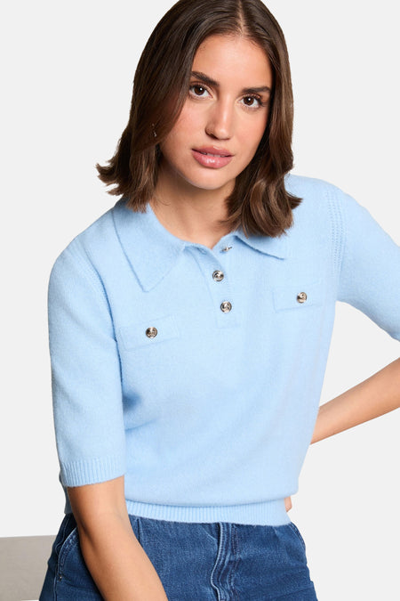 Blauwe trui van Morgan De Toi, met korte mouwen, kraag en zilverkleurige knopen, gecombineerd met een jeans.
