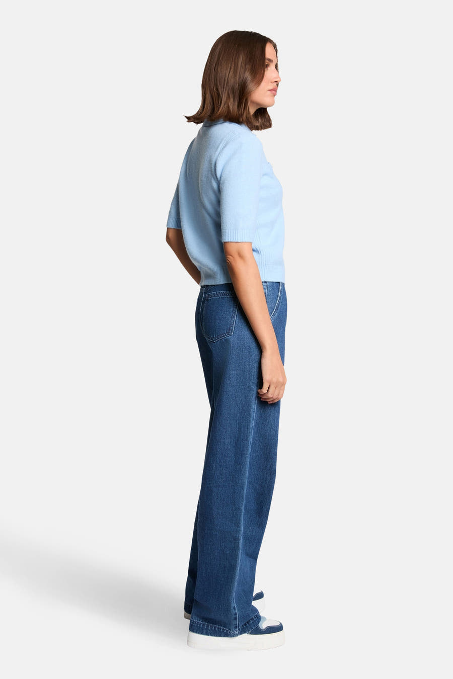 Blauwe trui van Morgan De Toi, gezien van opzij, met wijde jeans en witte sneakers.
