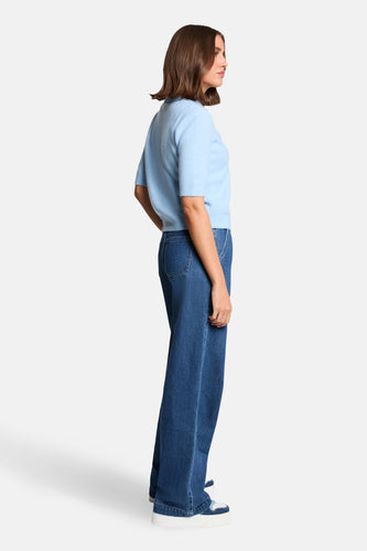 Blauwe trui van Morgan De Toi, gezien van opzij, met wijde jeans en witte sneakers.
