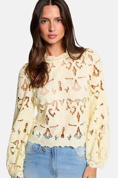 Gele blouse met lange mouwen van Morgan De Toi, met kanten details en gecombineerd met een blauwe jeans.
