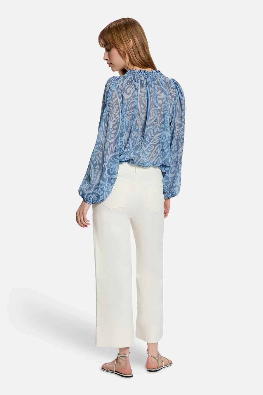 Blauwe blouse met lange mouwen van Morgan De Toi, met paisley patroon en gerimpelde halslijn, gecombineerd met witte broek en zilveren sandalen.
