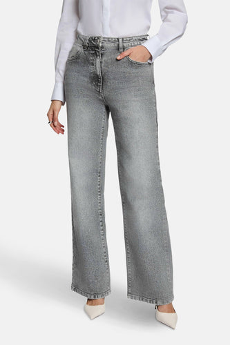 Grijze jeans met wijde pijpen, witte blouse, puntige pumps.