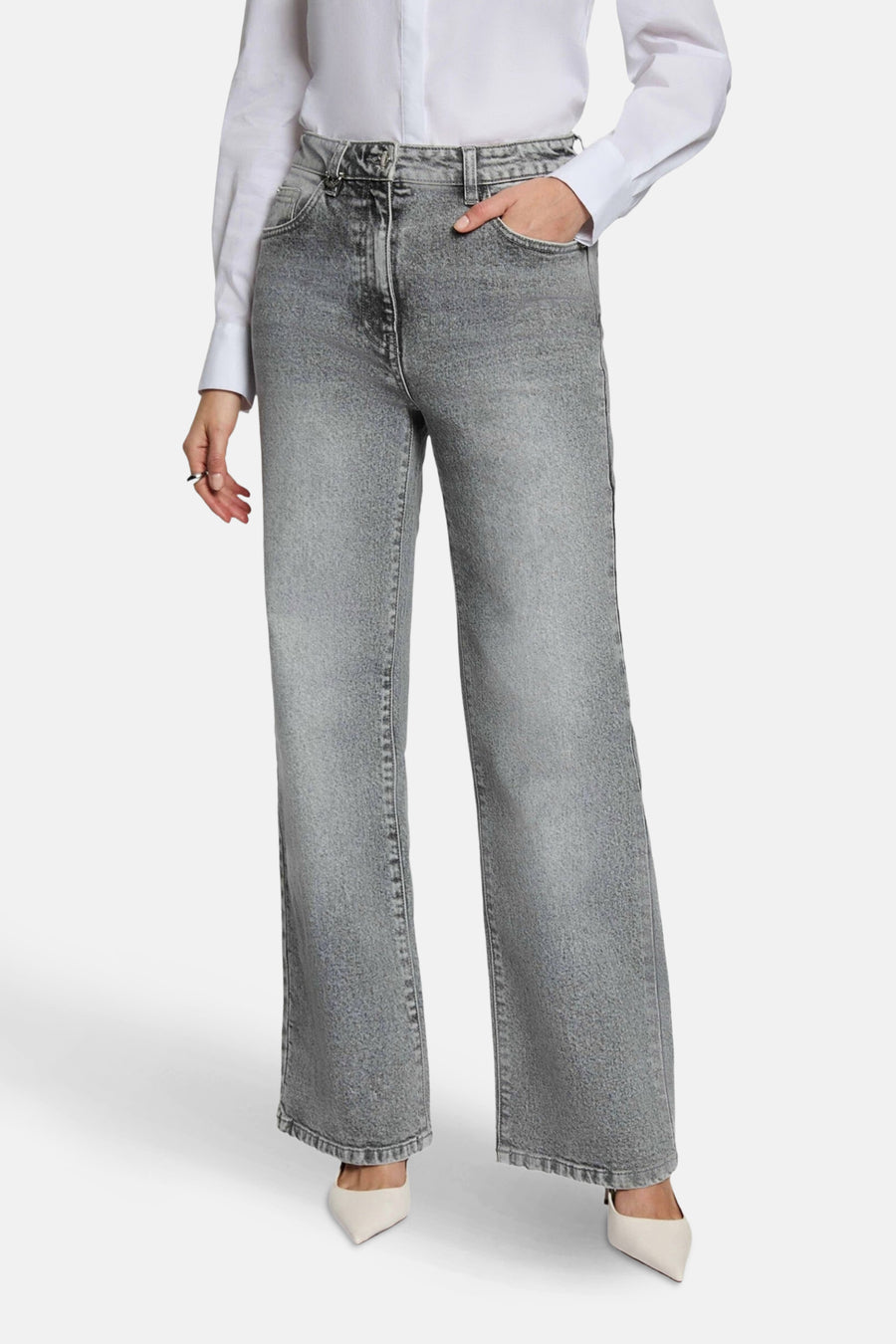 Grijze jeans met wijde pijpen, witte blouse, puntige pumps.