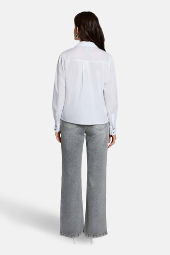 Achterkant van een vrouw in een wit overhemd en grijze jeans.