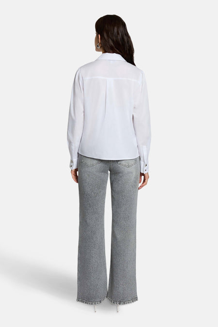 Achterkant van een vrouw in een wit overhemd en grijze jeans.