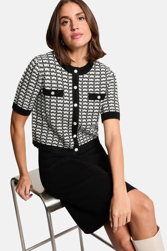 Zwarte jurk met korte mouwen van Morgan De Toi, gecombineerd met een zwart-wit jasje met knopen.
