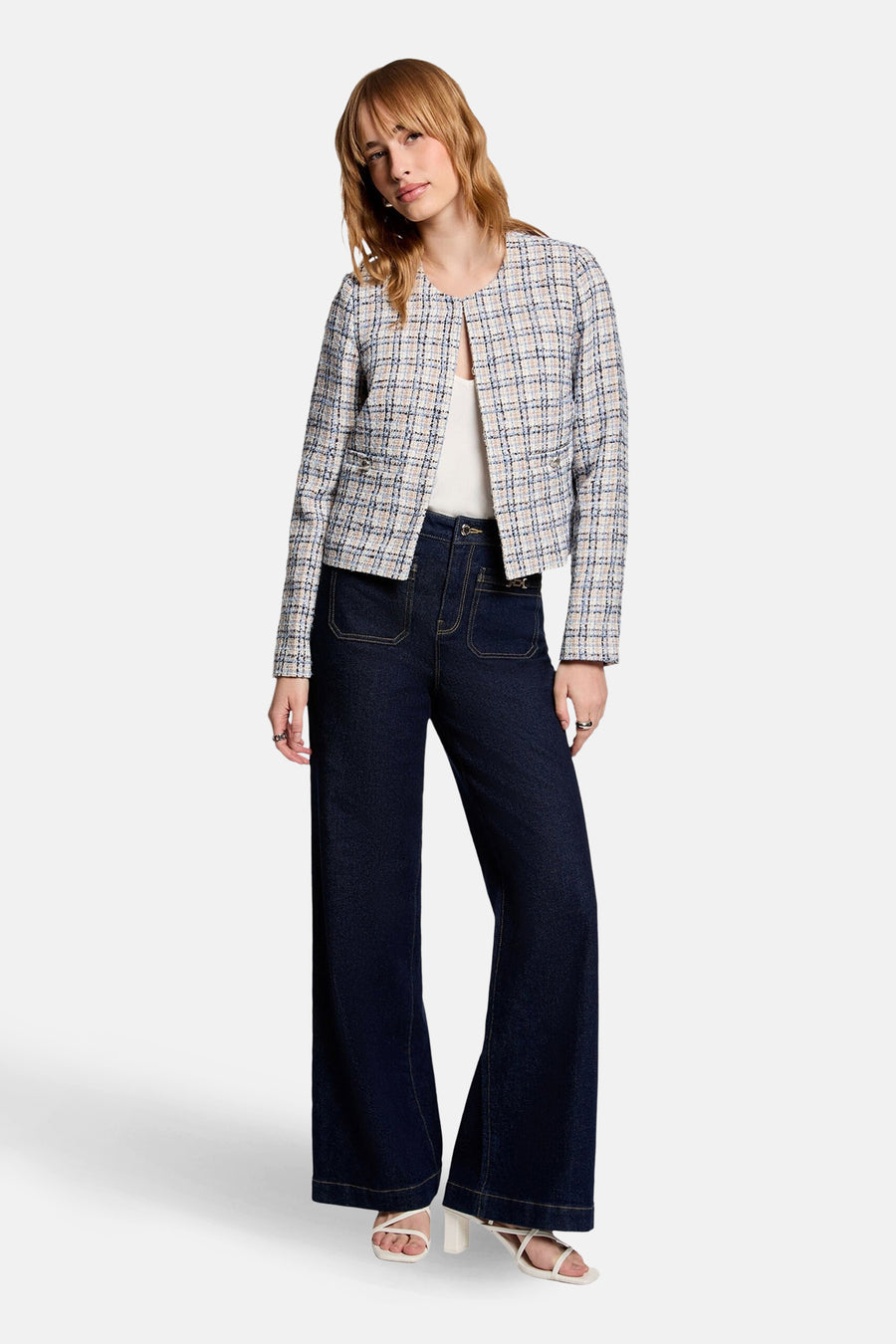 Blauw kort jasje van Morgan De Toi, met een geruit patroon, gedragen met wijde pijpen jeans en witte hakken.
