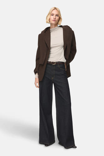 T-shirt beige à manches longues de MANGO, porté sous un blouson marron et des jeans bleus foncés larges.
