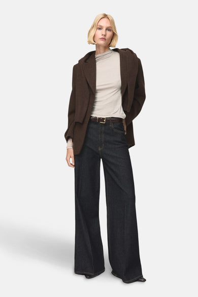 T-shirt beige à manches longues de MANGO, porté sous un blouson marron et des jeans bleus foncés larges.