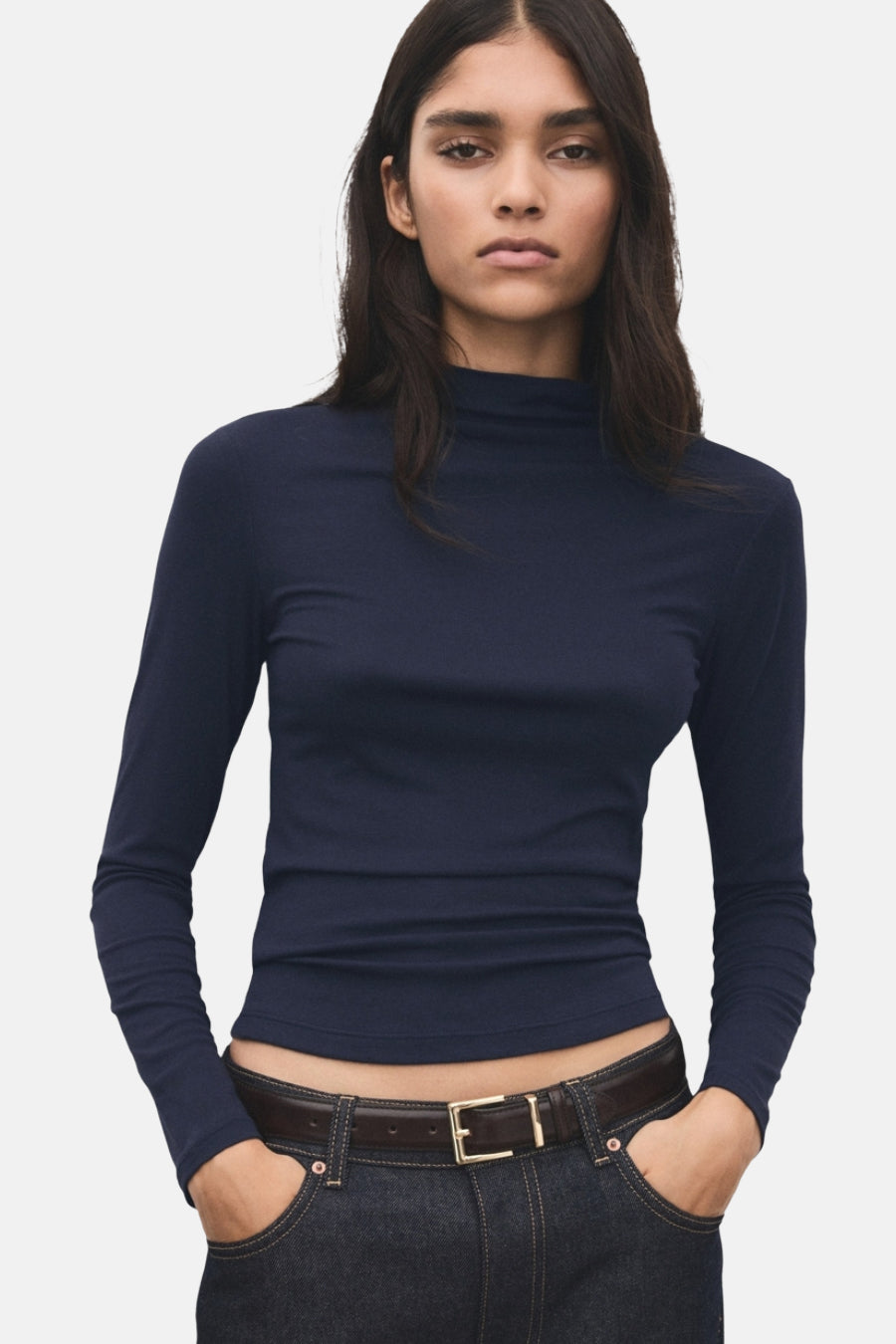 T-shirt bleu à manches longues de MANGO, vu par derrière, associé à un pantalon foncé et une ceinture marron.