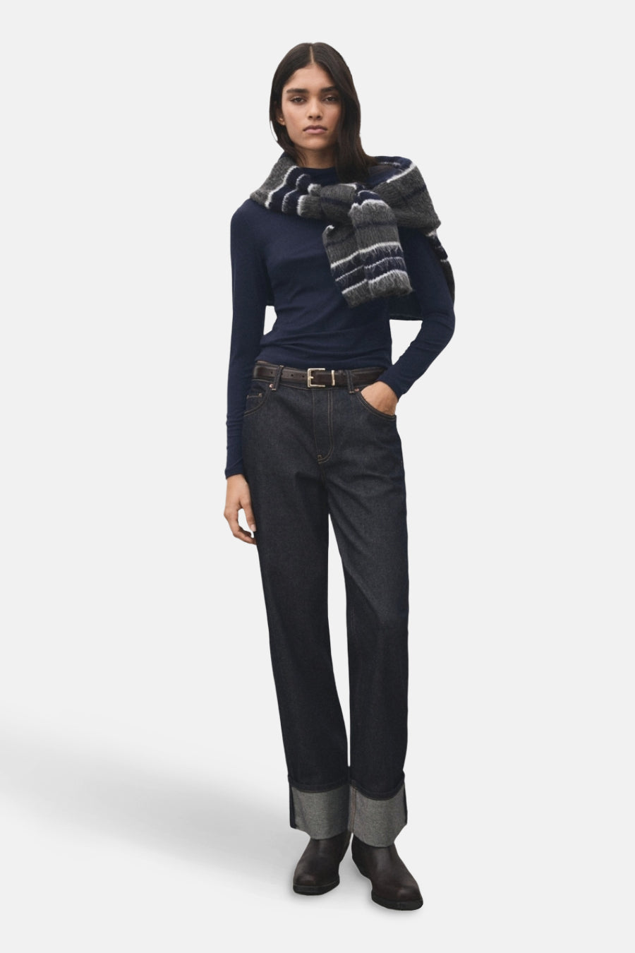T-shirt bleu à manches longues de MANGO, associé à un foulard rayé porté négligemment sur les épaules, combiné avec des jeans foncés et une ceinture marron.
