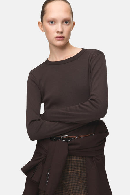 Bruin T-shirt met lange mouwen van MANGO, met gekruiste armen en een bruine jas om de taille geknoopt.